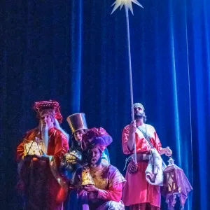 four men clumped together. One holds a star lamp high above their heads.